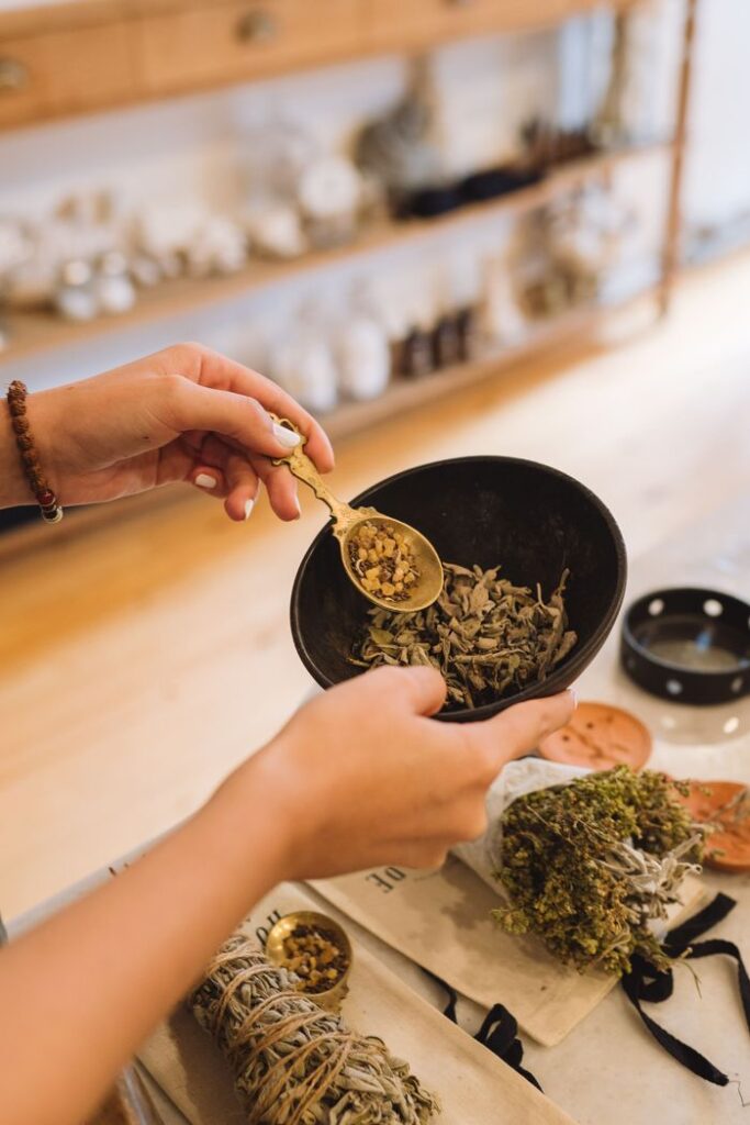 Hands holding herbs in a bowl, preparing incense in a cozy indoor setting.